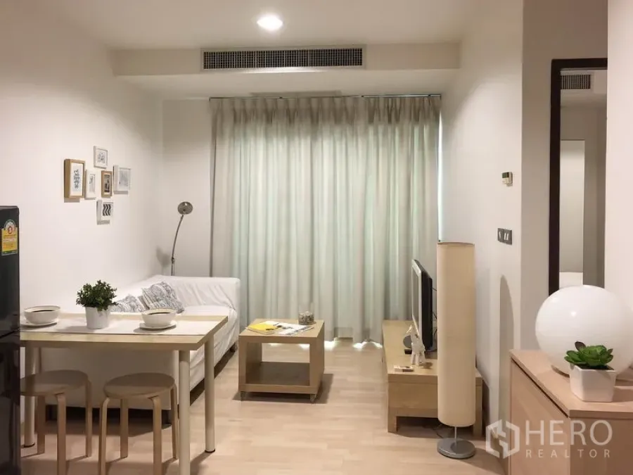 公寓 出租或出售在Watthana, Bangkok - 从入口望向客厅，见餐桌、沙发、电视柜、落地窗帘与中央空调出风口。
