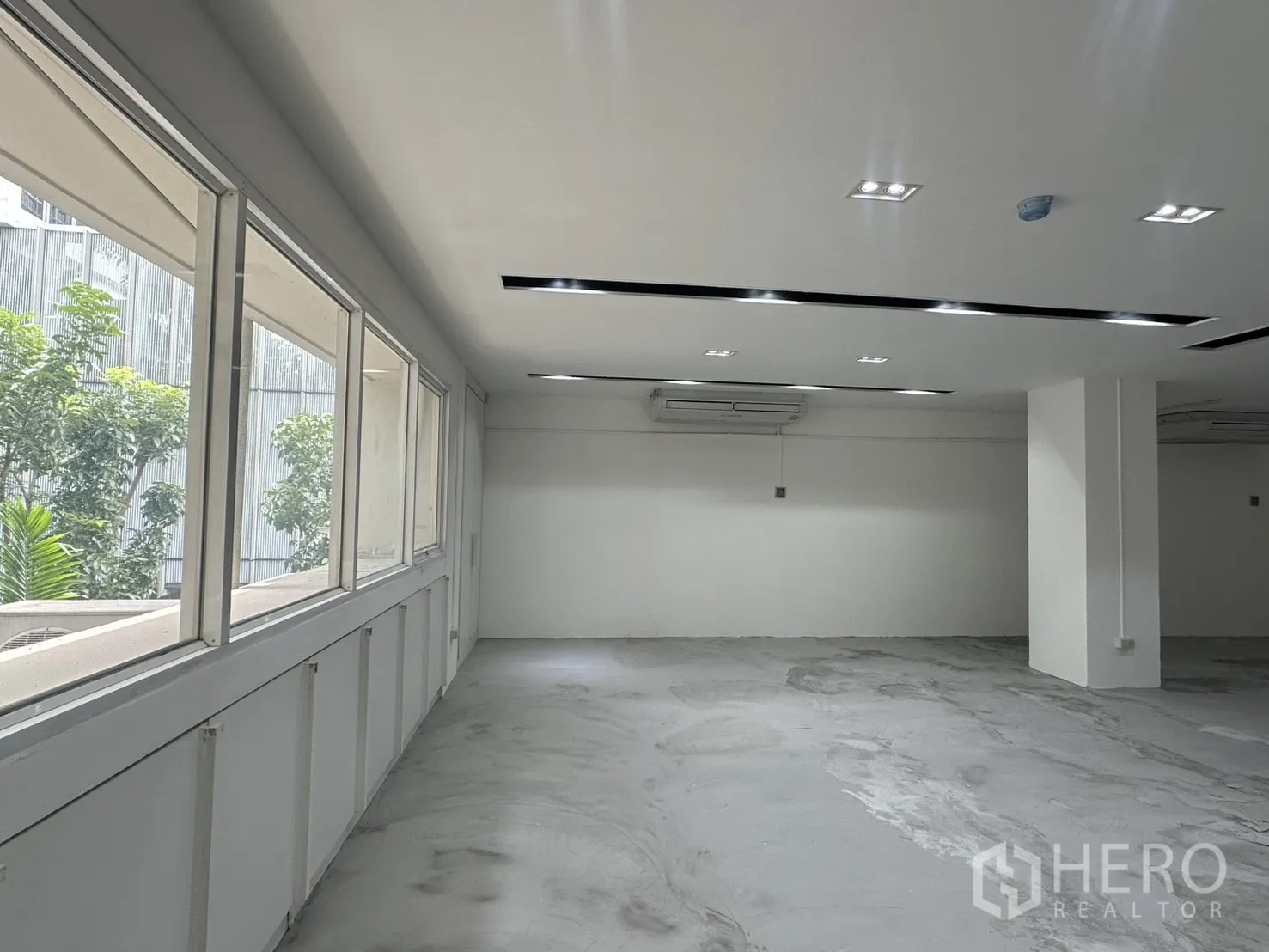 办公室 for rent in Pathum Wan, Bangkok - 一排大窗望向绿植，配壁挂分体空调与立柱。