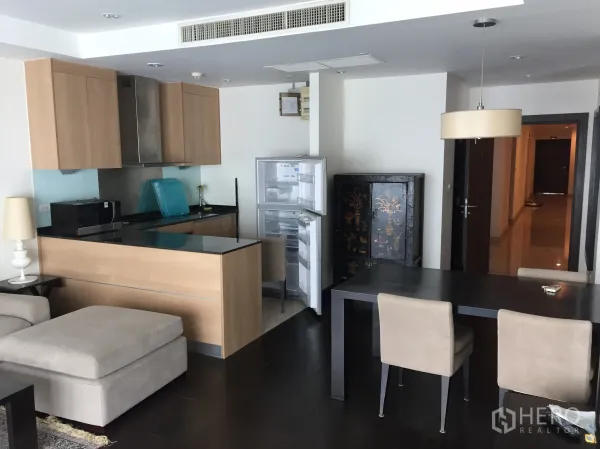 Condominium for rent in Sathon, Bangkok - Open-plan kitchen with wood cabinets and breakfast bar beside a dining table and open refrigerator.