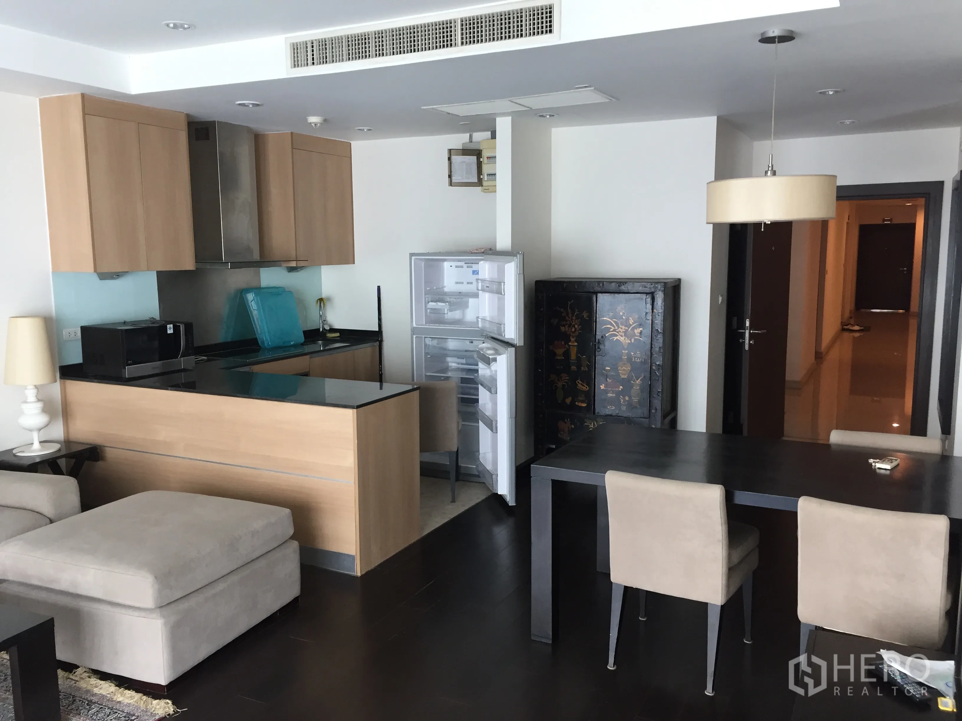 Condominium for rent in Sathon, Bangkok - Open-plan kitchen with wood cabinets and breakfast bar beside a dining table and open refrigerator.