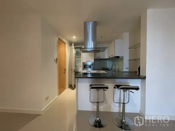 Condominium for rent or sale in Watthana, Bangkok - Compact kitchen with breakfast bar, two stools, stainless steel hood, and built-in appliances.