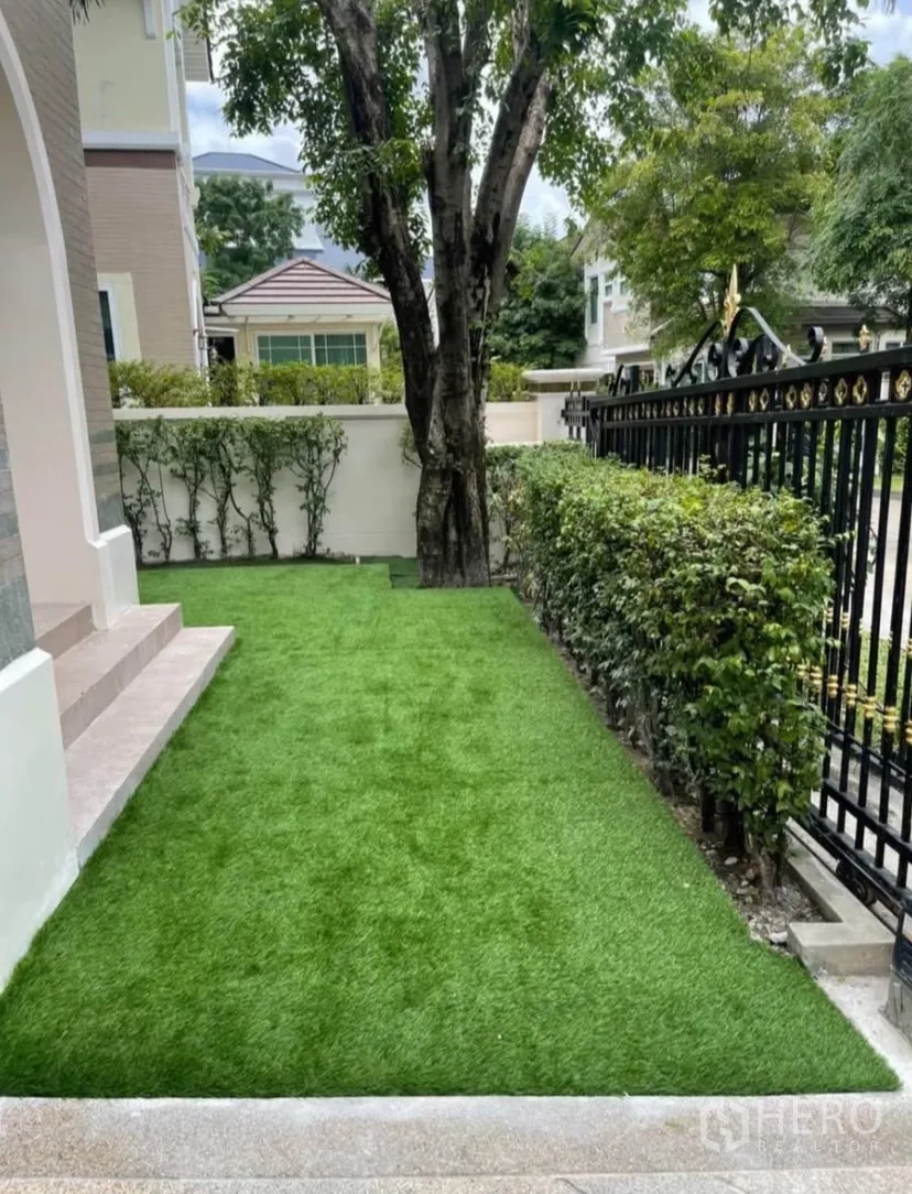 Detached House for rent or sale in Lat Phrao, Bangkok - Front garden with neat lawn, shade tree and black metal fence.