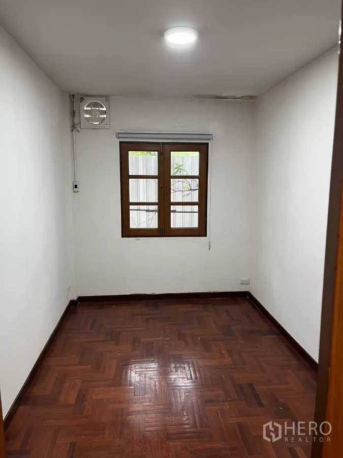 Detached House for rent in Watthana, Bangkok - Compact bedroom with parquet floor, white walls and a wooden-framed window.