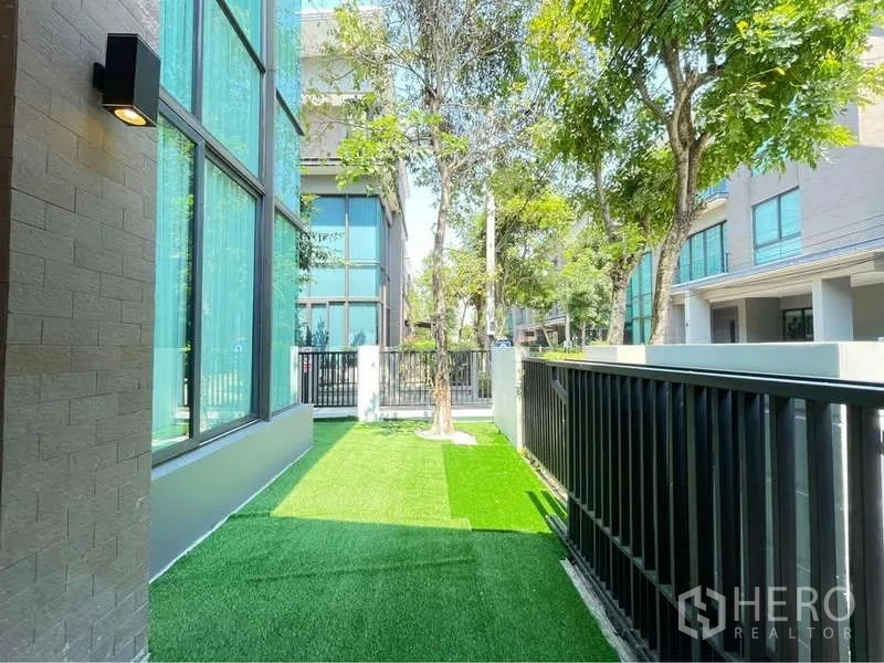 独立式住宅 出租在Bang Sue, Bangkok - 侧院人造草坪，树木与黑色金属围栏