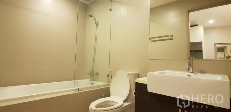 Condominium for rent in Khlong Toei, Bangkok - Modern bathroom with bathtub, glass shower screen and wide vanity.