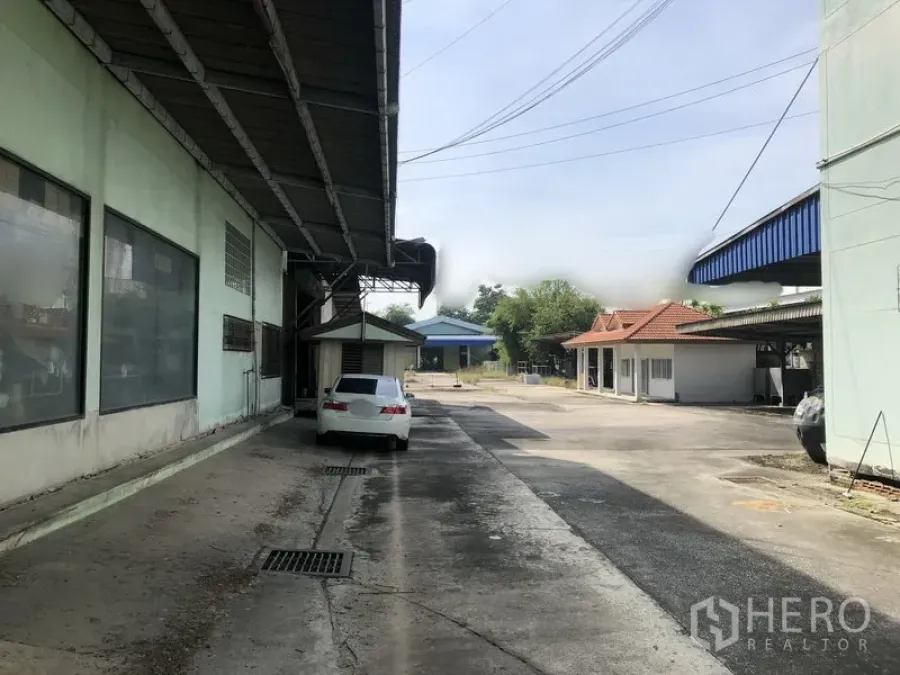 Warehouse for rent or sale in Lam Luk Ka, Pathum Thani - Covered loading lane beside the warehouse with a driveway and a parked car.