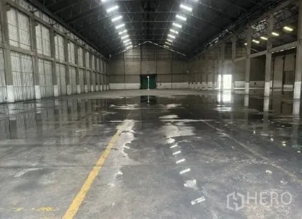 Warehouse for rent in Mueang Pathum Thani, Pathum Thani - Wide warehouse bay with reflective concrete floor, central access door, and ceiling lights.