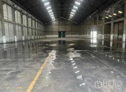 Warehouse for rent in Mueang Pathum Thani, Pathum Thani - Wide warehouse bay with reflective concrete floor, central access door, and ceiling lights.