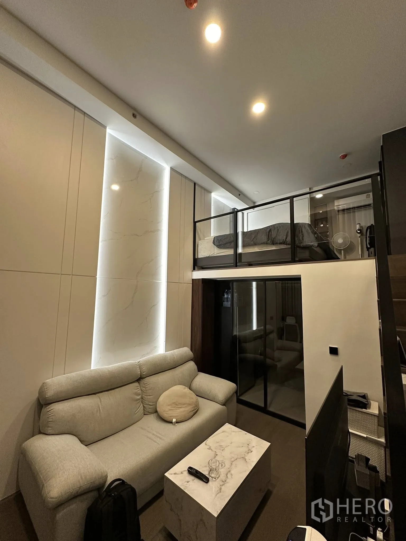 公寓 出租在Bang Rak, Bangkok - 阁楼式卧区位于客厅上方，玻璃护栏与筒灯，下方为沙发和茶几。