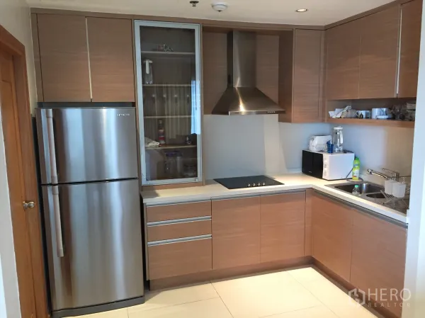 Condominium for rent in Khlong Toei, Bangkok - Modern L-shaped kitchen with stainless refrigerator, cooktop, range hood and ample cabinetry.