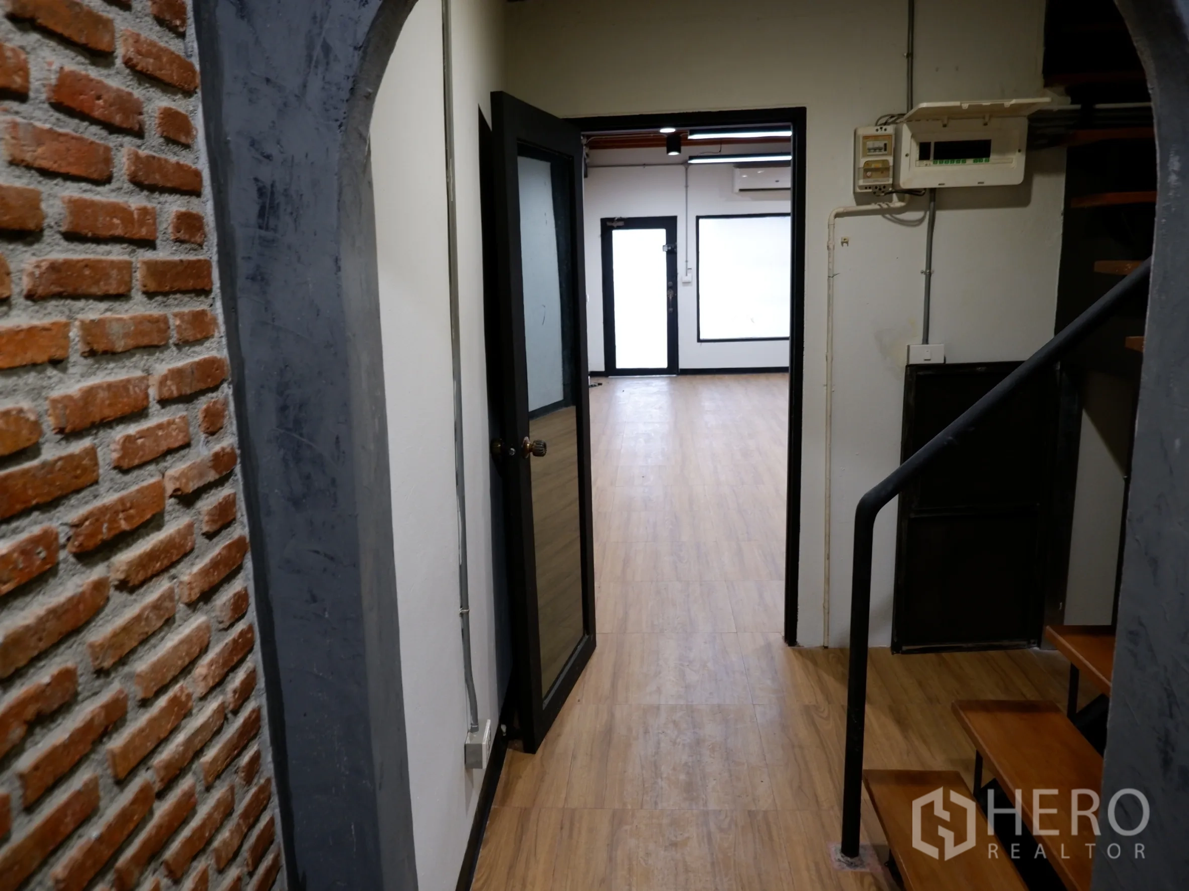 带办公室的家 出售在Bang Rak, Bangkok - 工业风走廊，裸砖墙、黑色金属楼梯与木纹地面。