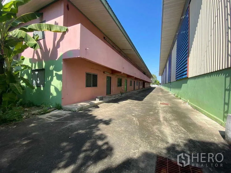 货栈 出租在Lat Lum Kaeo, Pathum Thani - 粉色宿舍建筑后侧，与仓库并排及混凝土步道。