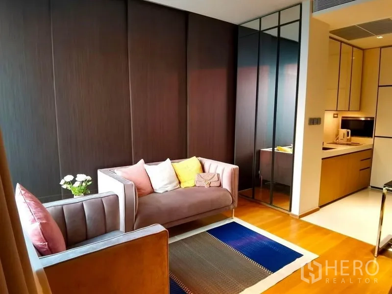 Condominium for rent in Khlong Toei, Bangkok - Modern living area with soft-tone sofas, dark feature wall, and built-in kitchenette.