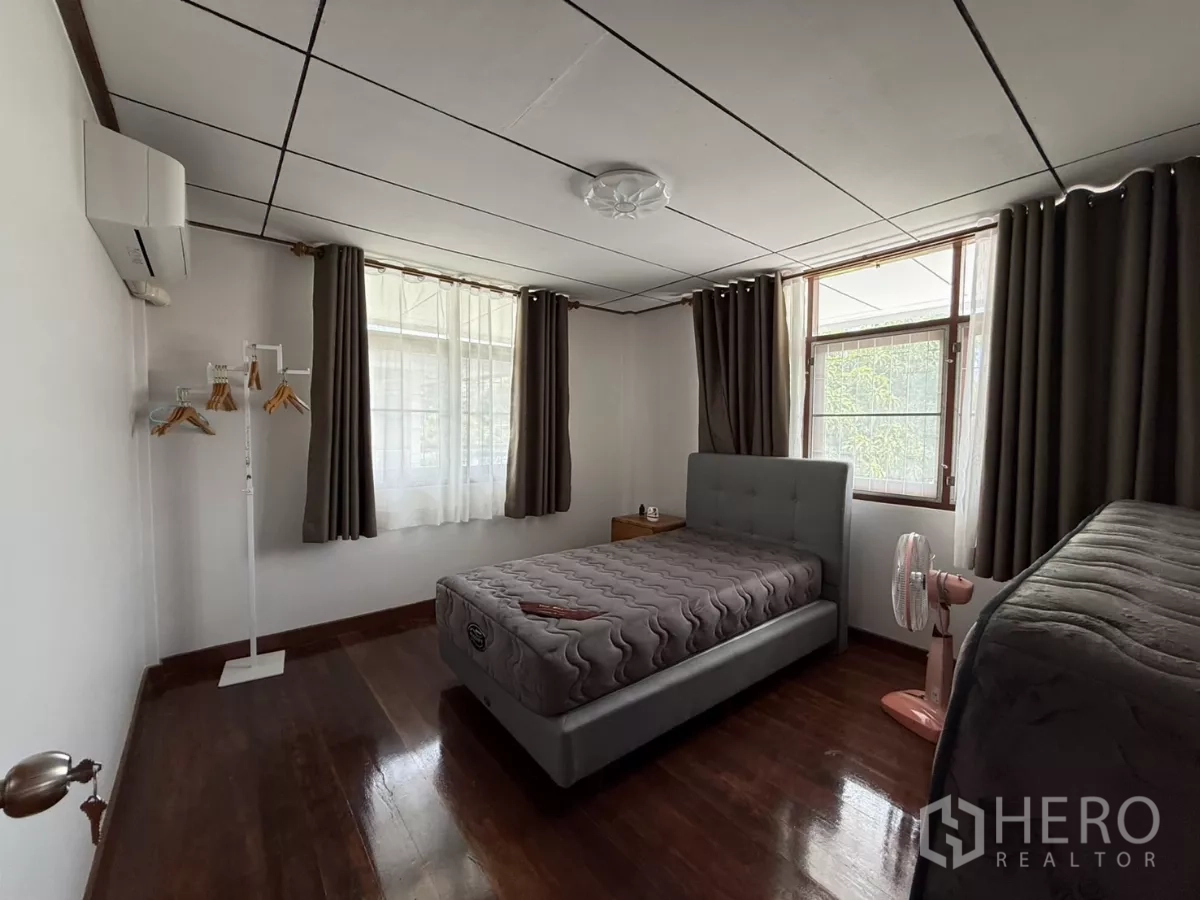 Detached House for rent in Phra Khanong, Bangkok - Upper-floor bedroom with bed, wide windows, curtains and wooden floor.