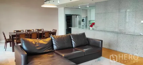 Condominium for sale in Sathon, Bangkok - Open-plan living and dining area with a black leather sofa, long dining table, and granite breakfast bar.