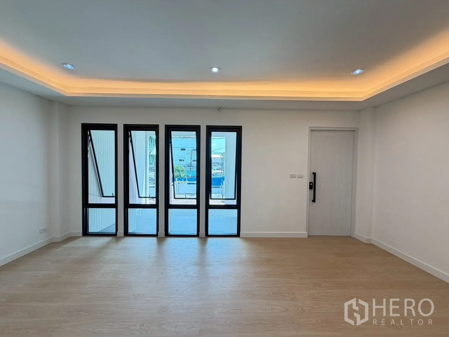 Townhouse for sale in Phra Khanong, Bangkok - Bright living area with wood-look floors, recessed ceiling lights, and tall windows.