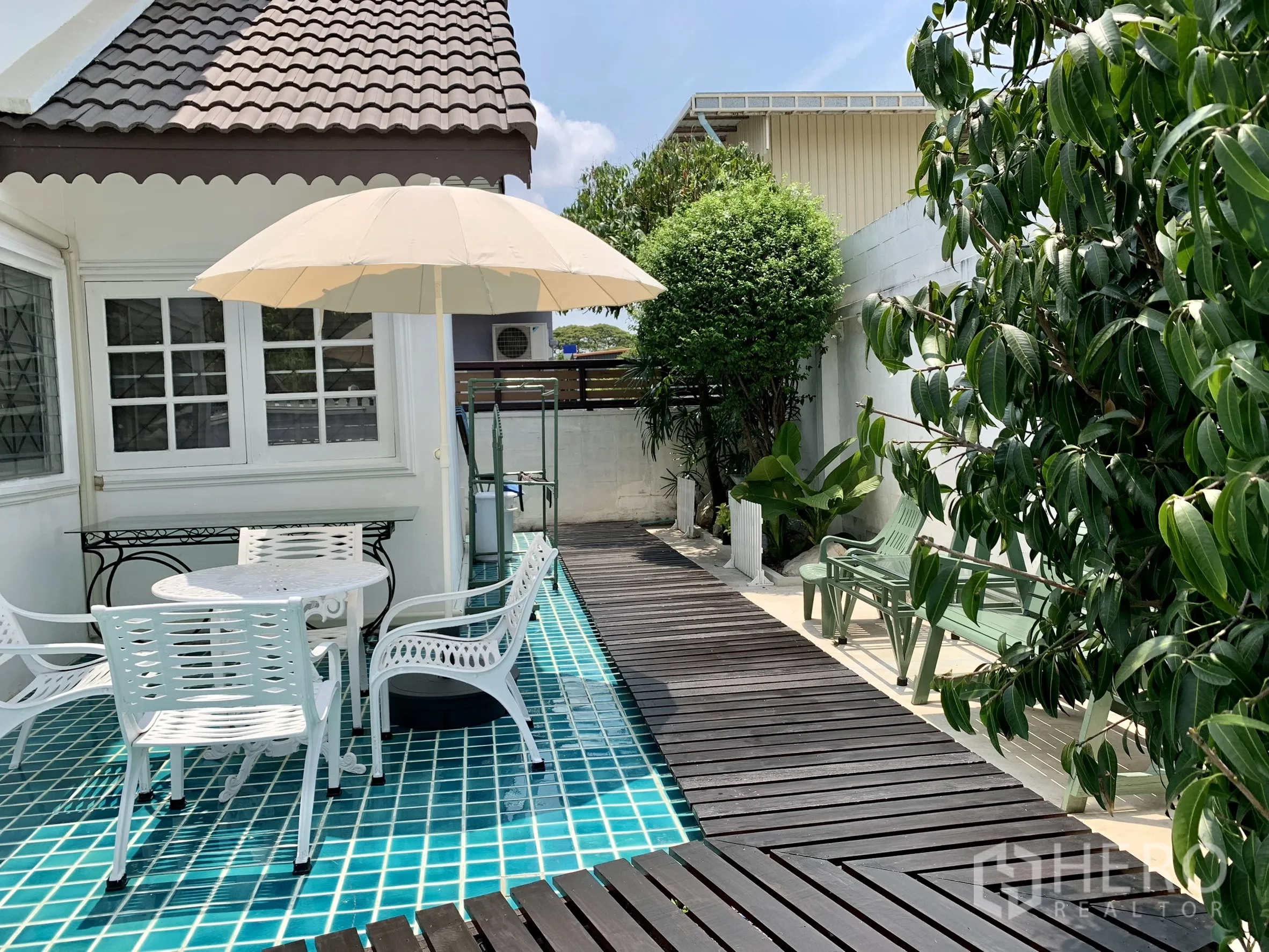 独栋房屋 for rent in Saphan Sung, Bangkok - 蓝绿色瓷砖露台与木栈道，圆桌、椅子、遮阳伞及绿植点缀。