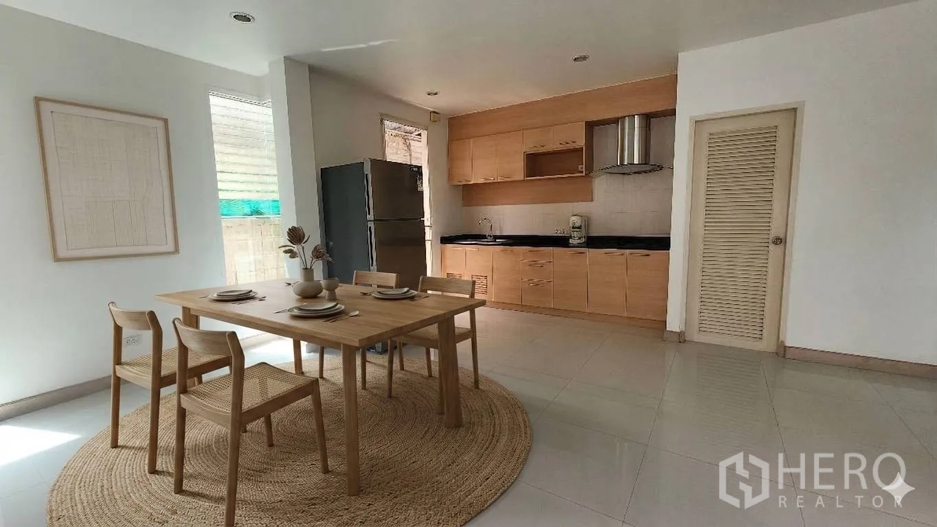 Detached House for rent in Watthana, Bangkok - Dining area with wooden table next to a built-in kitchen and refrigerator.