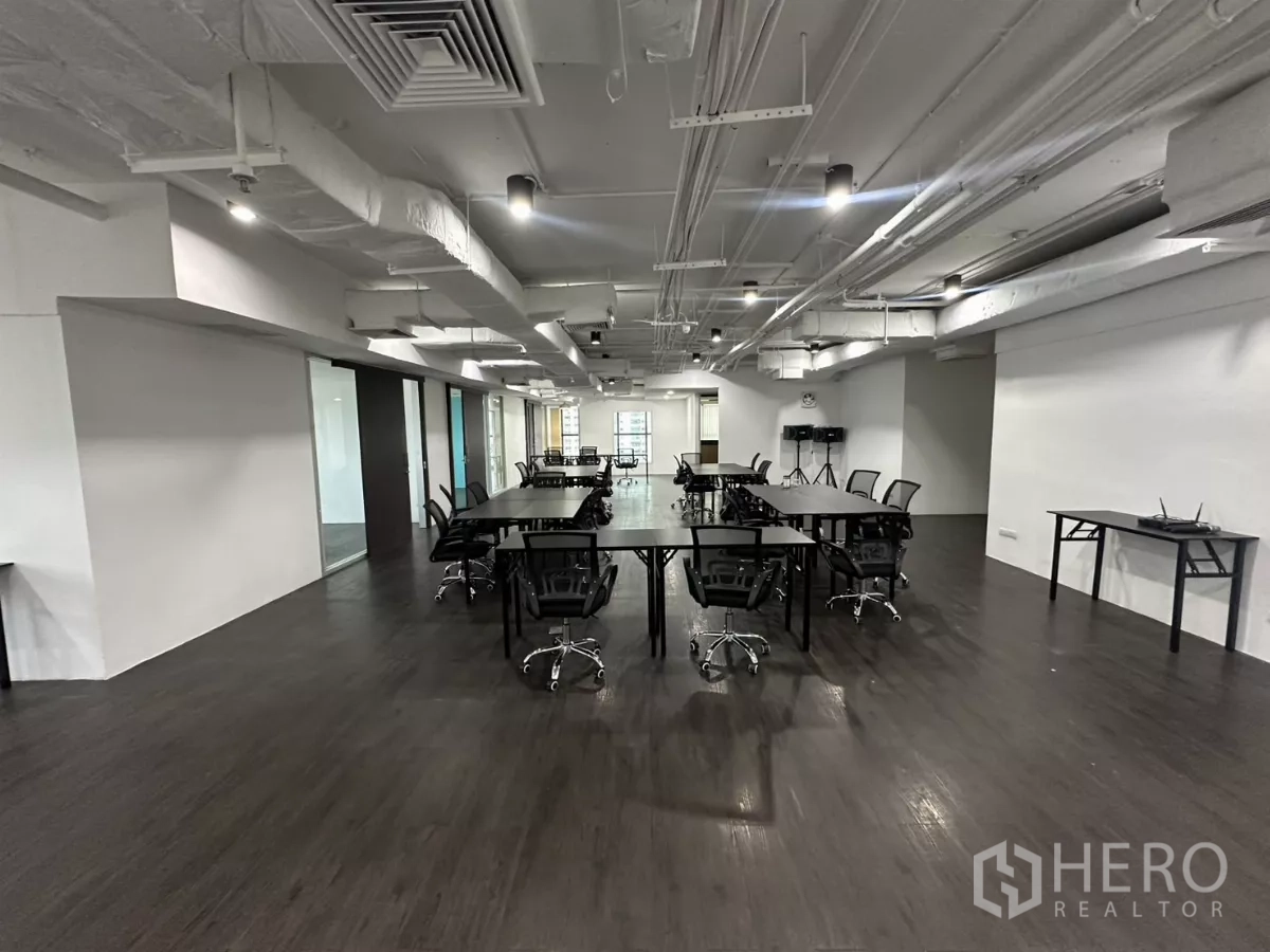 Office Space for rent in Watthana, Bangkok - Long workspace with rows of desks, glass-partitioned rooms and bright ceiling lights.
