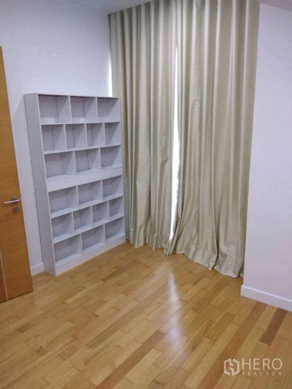 Condominium for rent in Khlong Toei, Bangkok - Bright second bedroom or study with shelving unit, full-height curtains, and wood flooring.