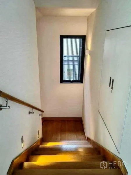 独立式住宅 出售在Huai Khwang, Bangkok - 木质楼梯带扶手与壁灯，侧窗引入自然光。