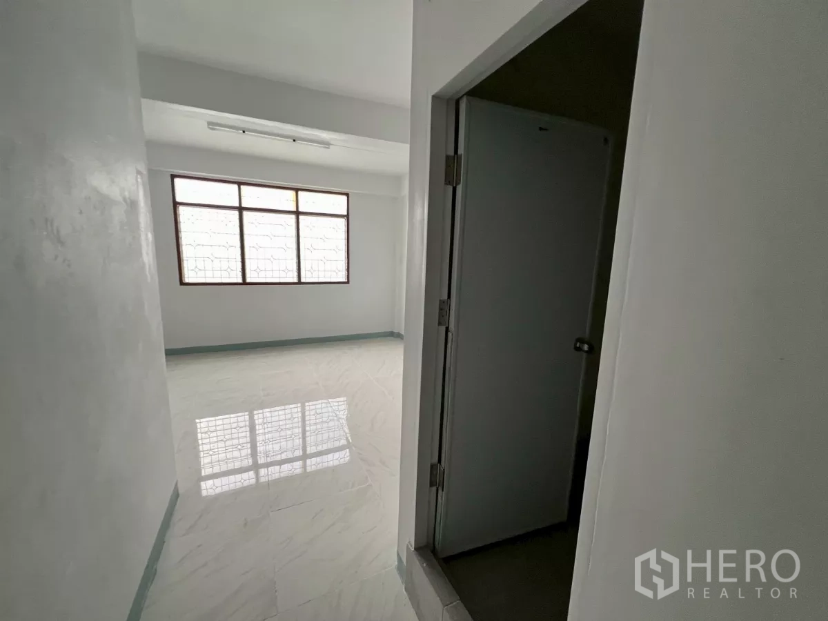 Shophouse for rent in Khlong Toei, Bangkok - Hallway leading to a bright tiled room with window, door frame visible in foreground.