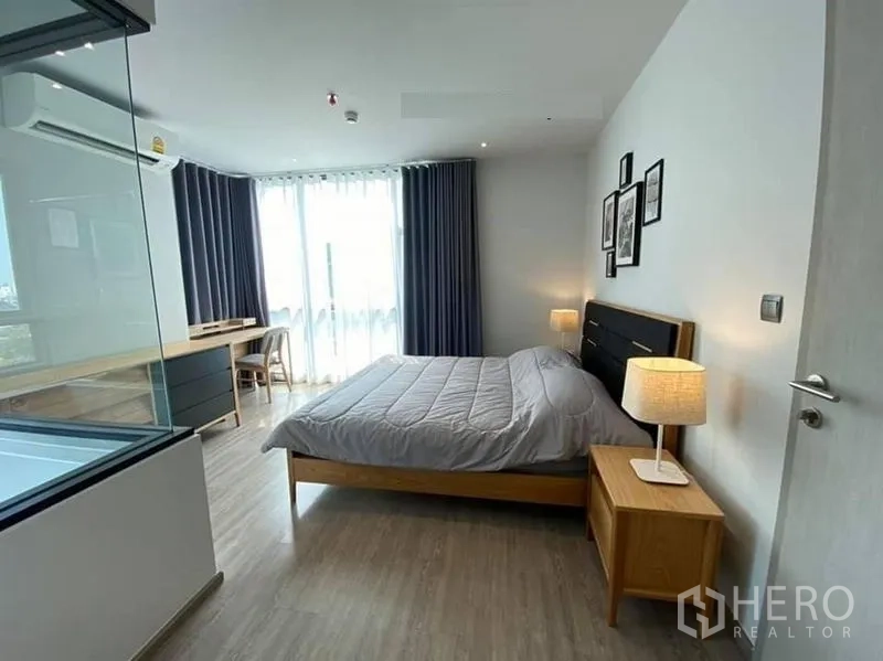 公寓 出租在Watthana, Bangkok - 主卧带书桌与转角落地窗，浴缸置于玻璃隔断后。