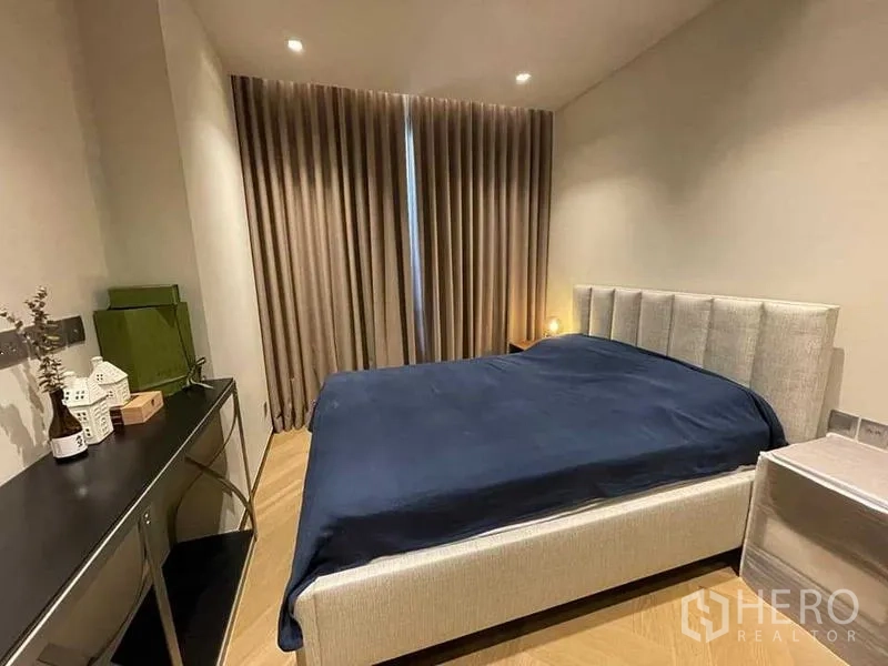 คอนโด ให้เช่าหรือขาย - ห้องนอนที่สองพร้อมเตียงบุนวม โต๊ะทำงาน และม่านทึบ