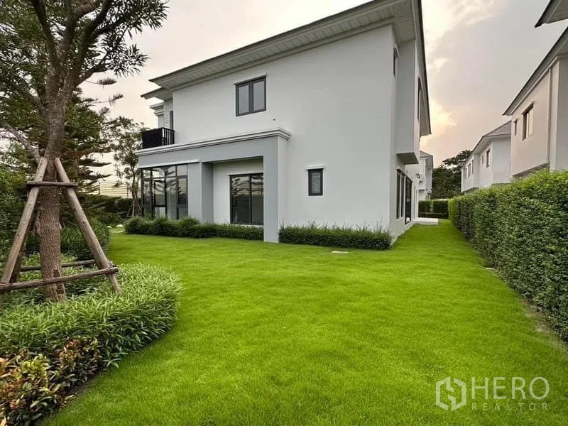 Detached House for sale in Lat Krabang, Bangkok - Two-storey modern detached house with white facade and expansive green lawn bordered by hedges.