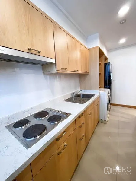 Condominium for rent - Linear kitchen with electric cooktop, marble-look countertop, wooden cabinetry and washer.