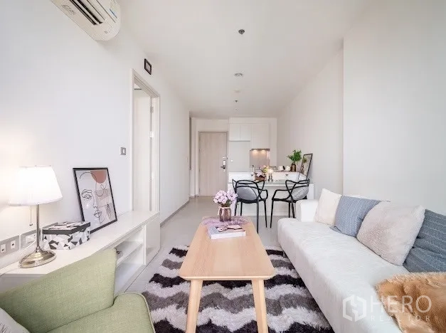Condominium for sale in Khlong Toei, Bangkok - Bright open-plan living and dining area with sofa, chevron rug, and compact kitchen in a Sukhumvit condo near BTS Ekkamai.