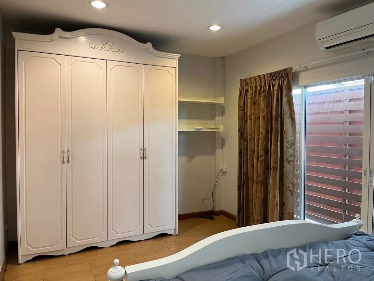 Townhouse for rent in Bang Kho Laem, Bangkok - Bedroom corner showing white wardrobe, shelves, and sliding glass door with wood screen.