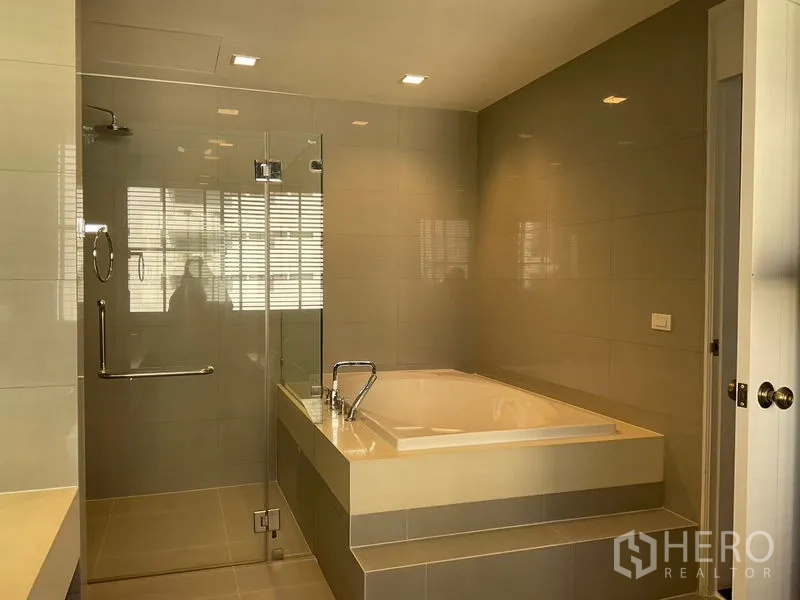 Apartment for rent in Sathon, Bangkok - Bathroom with glass shower enclosure and raised soaking tub.