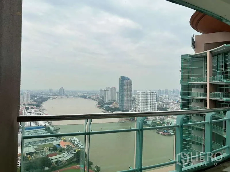 Condominium for rent in Bang Kho Laem, Bangkok - Covered balcony with glass railing facing the Chao Phraya River and nearby tower.