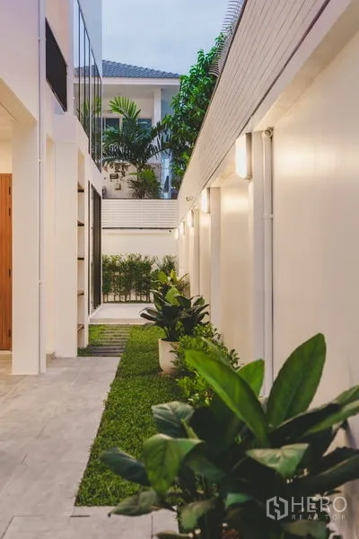 Townhouse for sale in Phra Khanong, Bangkok - Landscaped side yard with potted greenery, pathway lighting and a white boundary wall.