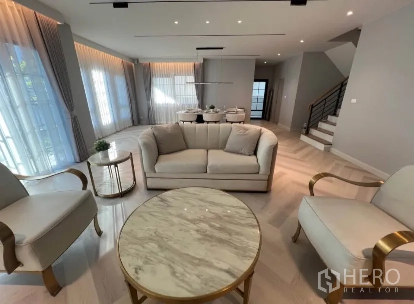 独栋房屋 for rent in Bang Phli, Samut Prakan - 优雅开放式客厅，沙发组与大理石茶几，连接餐区与楼梯，落地窗帘环绕。