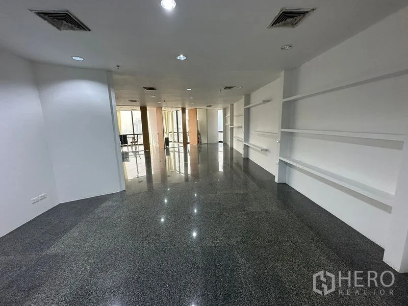 Office Space for rent - Open workspace with dark stone flooring, downlights and display shelving leading to meeting rooms.