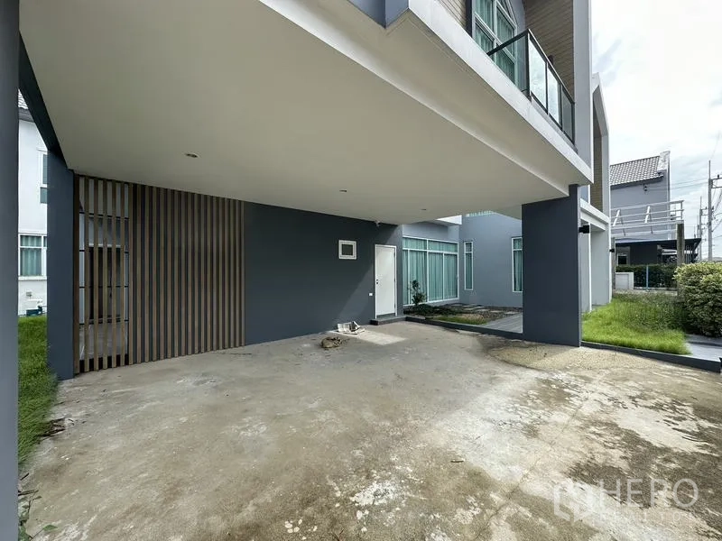 Detached House for sale in Lam Luk Ka, Pathum Thani - Covered two-car carport beneath a cantilevered upper floor beside a small lawn.