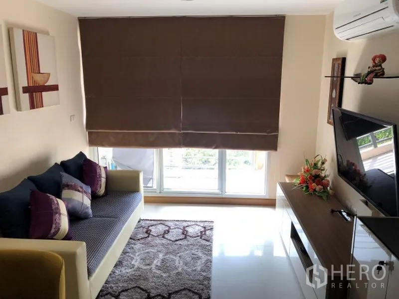 Condominium for rent in Khlong Toei, Bangkok - Living room with large window and blackout blinds, sofa, TV unit, and area rug.