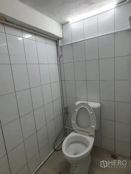 Shophouse for rent in Phra Khanong, Bangkok - White-tiled restroom with toilet and handheld bidet spray under bright lighting.