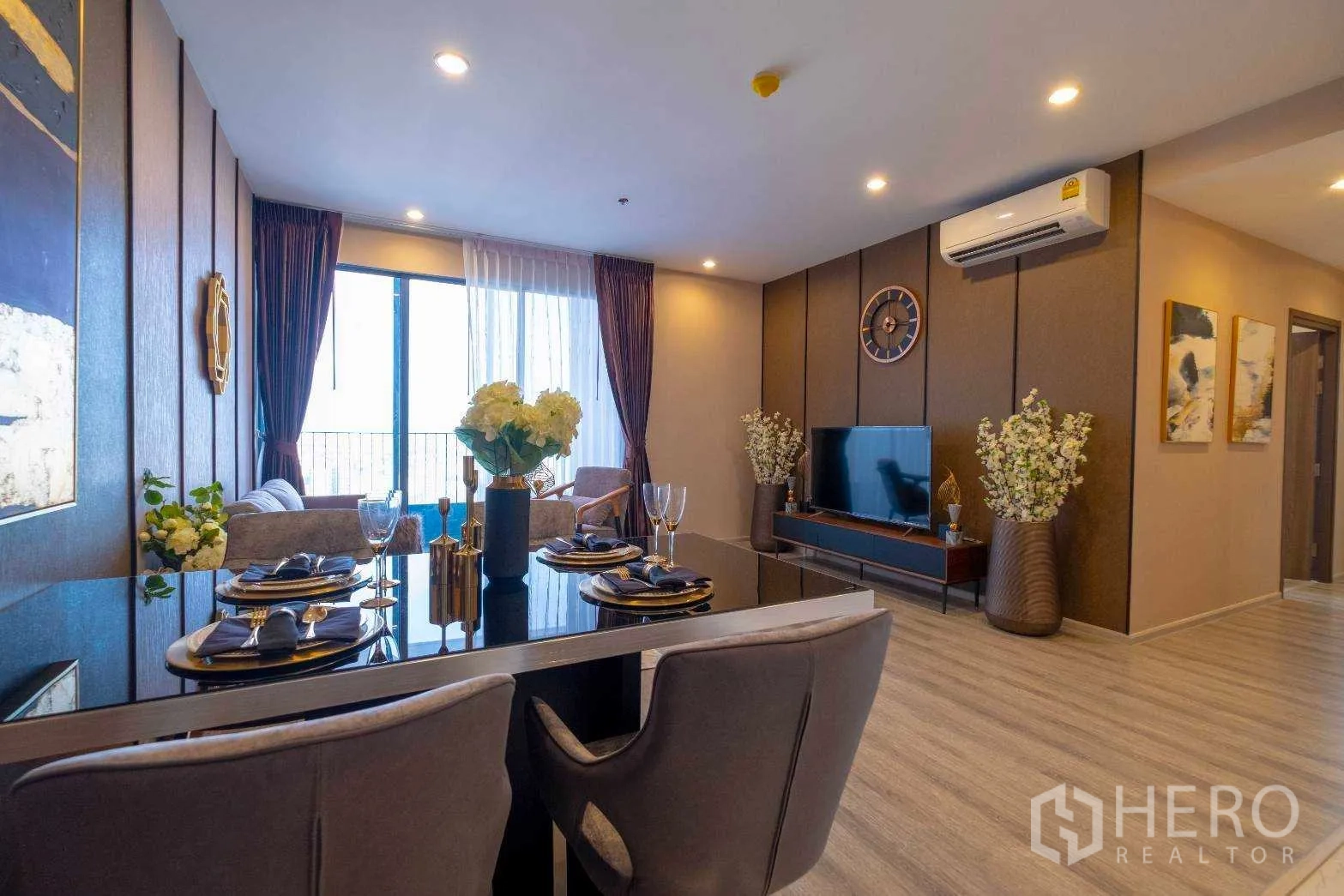 公寓 出租在Bang Na, Bangkok - 开放式餐客一体，深色餐桌、电视墙与推拉门通向阳台。