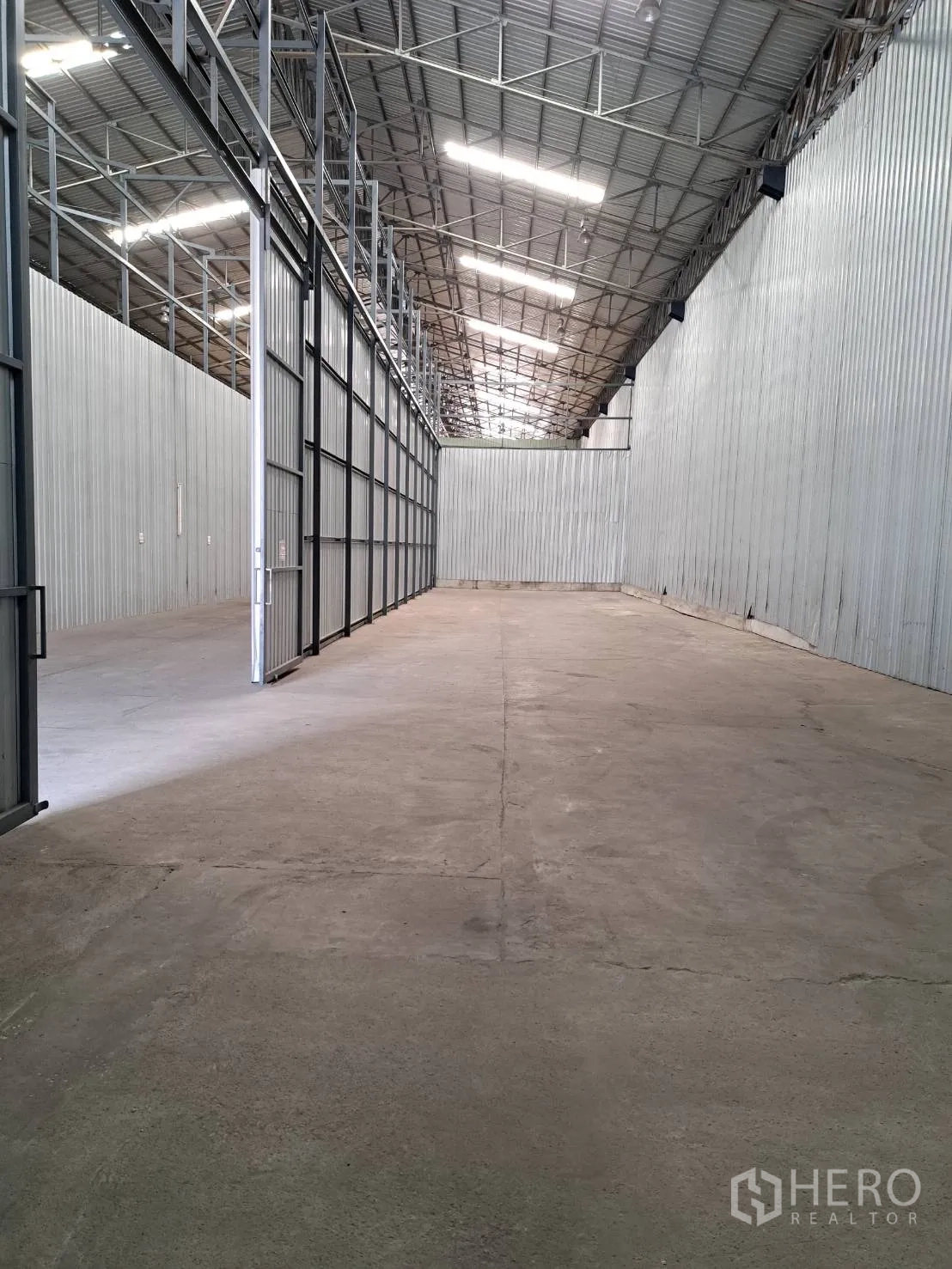 Warehouse for rent in Pak Kret, Nonthaburi - Spacious warehouse interior with high metal truss roof, bright skylights, corrugated steel walls, and smooth concrete floor.