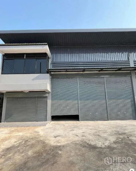 Warehouse for rent in Phra Samut Chedi, Samut Prakan - Modern warehouse exterior with an upper-floor glass office, multiple steel roller shutters, and a wide concrete loading forecourt.