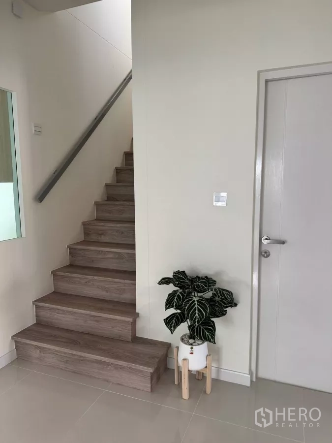 独立式住宅 出租在Bang Phli, Samut Prakan - 室内楼梯，木质踏步与金属扶手，旁有白门与盆栽。
