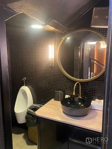 Shophouse for rent - Contemporary men’s restroom with round mirror, vessel sink, and tiled walls.
