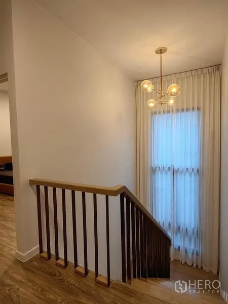 Detached House for rent in Bang Kapi, Bangkok - Wood staircase with sleek balustrade and pendant chandelier beside a tall curtained window