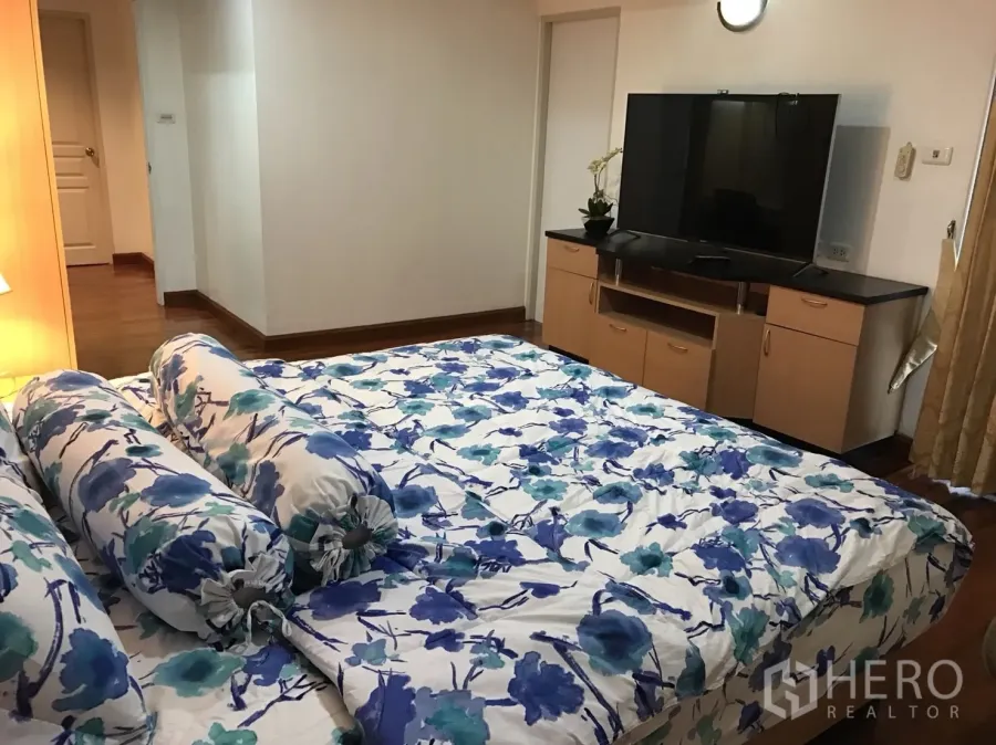 Condominium for rent in Khlong Toei, Bangkok - Cozy master bedroom with floral bedding, TV console and warm wood floors.