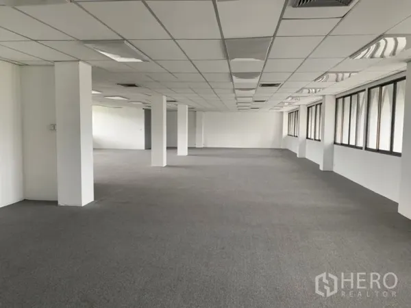 Office Space for rent in Ratchathewi, Bangkok - Long rectangular office space with multiple columns, carpet flooring, and rows of windows providing abundant natural light.