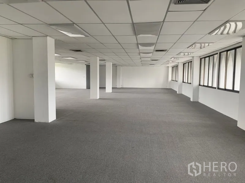 Office Space for rent in Ratchathewi, Bangkok - Long rectangular office space with multiple columns, carpet flooring, and rows of windows providing abundant natural light.