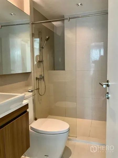 Condominium for sale in Khlong Toei, Bangkok - Modern bathroom with glass-enclosed shower, vanity and neutral tiled walls.